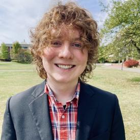 Peter Watko, wearing a black jacket and plaid shirt, smiling outdoors