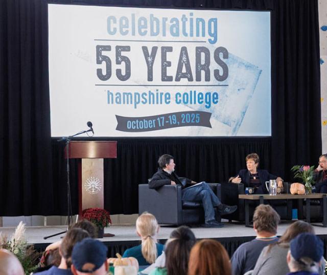 Ken Burns, Lynn Pasquerella, and Gary Marcus sit on a stage under a banner reading Celebrating 55 Years