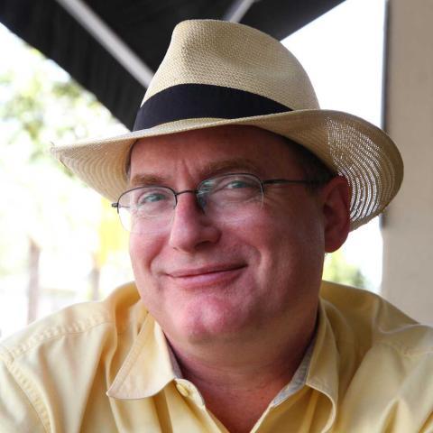 Dan-Epstein-76F smiles at the camera wearing a hat and yellow shirt.