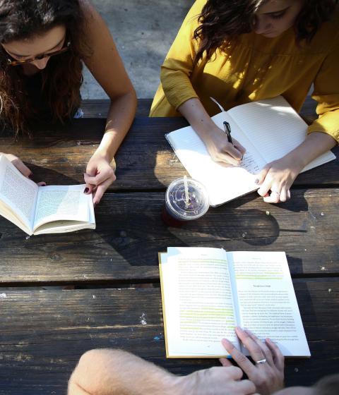 Three people writing on a picnic table.